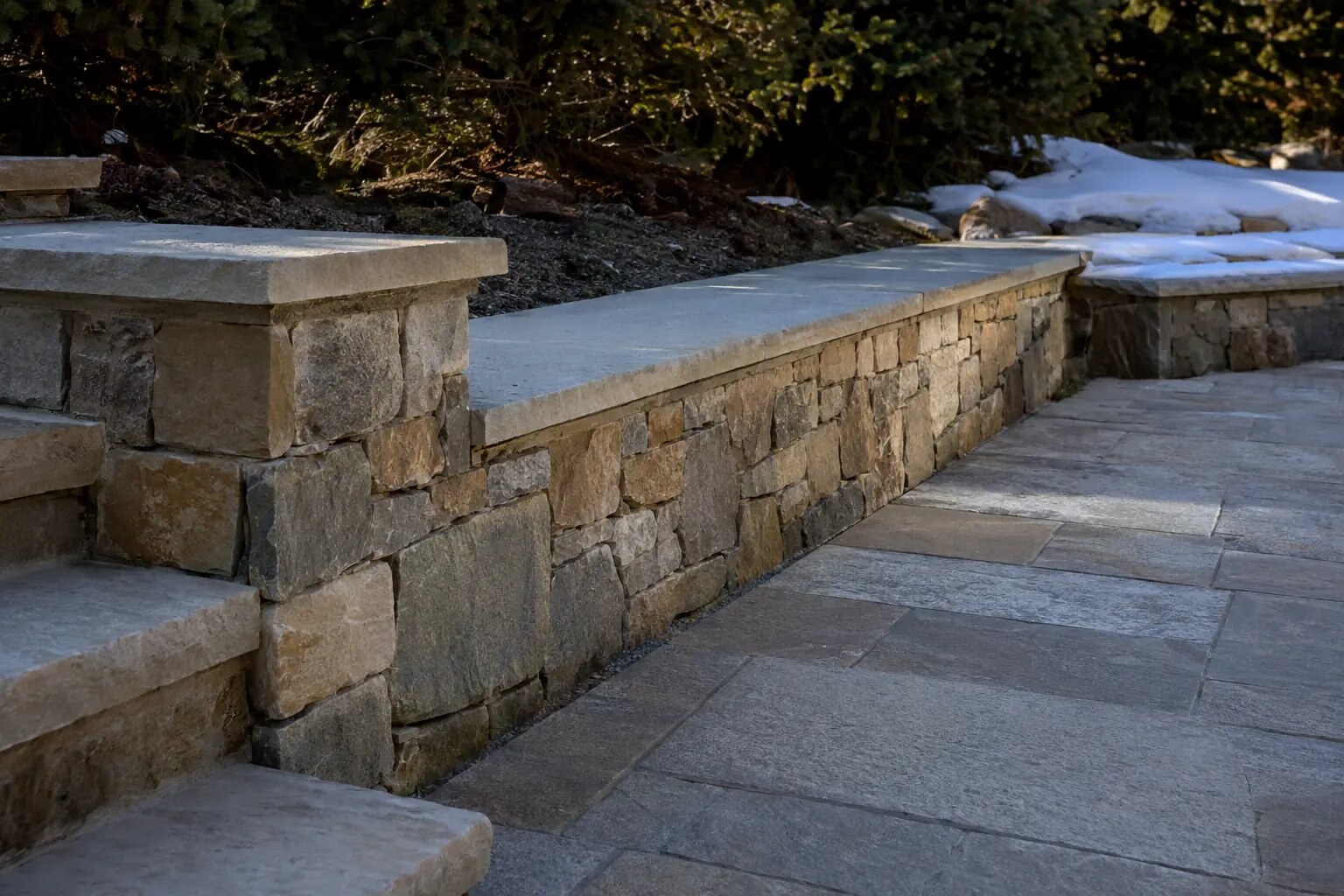 Illustrative natural-stone terrace showing varied stone, cap slope, joints, drainage edge, and adjacent paving